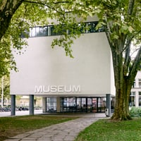 Aussenansicht eines modernen Gebäudes mit Museumsschild und Bäumen.