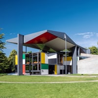 Modernes, farbenfrohes Gebäude mit grossen Überhängen und Glasfassade im Grünen.",