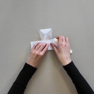 Hände falten einen Stuhl aus Papier auf grauem Hintergrund.