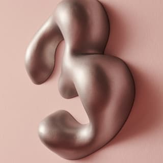 Silberne abstrakte Skulptur vor rosa Hintergrund.