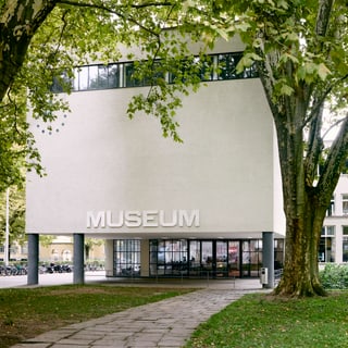 Aussenansicht eines modernen Gebäudes mit Museumsschild und Bäumen.