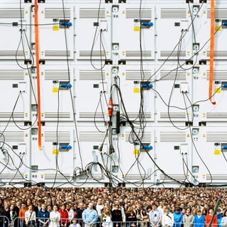 Menschenmenge vor technischer Wand mit Kabeln.