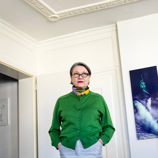 Frau in grünem Pullover steht in einem weissen Raum mit Gemälde an der Wand.