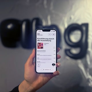 Hand hält Smartphone vor unscharfem Hintergrund mit Schriftzug 'ping!'.