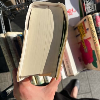 Hand hält ein geöffnetes Buch über einem Tisch mit Büchern.