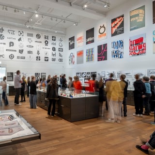 Besucher in einer Galerie mit Kunstwerken und Logos an den Wänden.