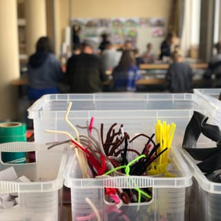 Materialien für Bastelarbeiten in einem Raum mit Menschen im Hintergrund.