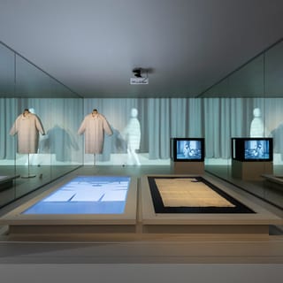 Museumsausstellung mit Kleidungsstücken und Bildschirmen.