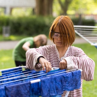 Kind hängt blaue Stoffe an Wäscheständer im Freien auf.