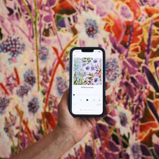 Hand hält Smartphone vor bunter Blumenwand.