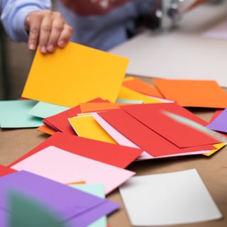 Hände von Kindern, die mit buntem Papier basteln.