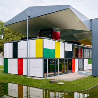 Modernes Gebäude mit bunten Fassadenpaneelen und grossen Fenstern im Grünen.