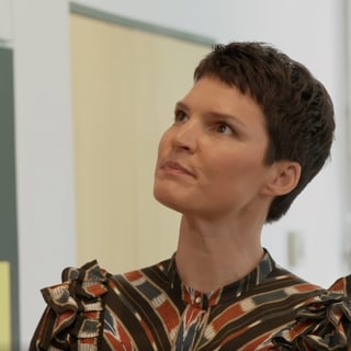 Person mit kurzem Haar blickt nachdenklich nach oben in einem Raum.