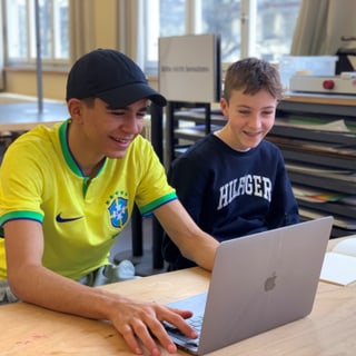 Zwei Jungen lachen und schauen auf einen Laptop Bildschirm.