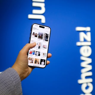 Hand hält Smartphone mit Fotos vor blauem Hintergrund.