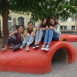 Vier Mädchen sitzen auf einer roten Skulptur auf einem Spielplatz.