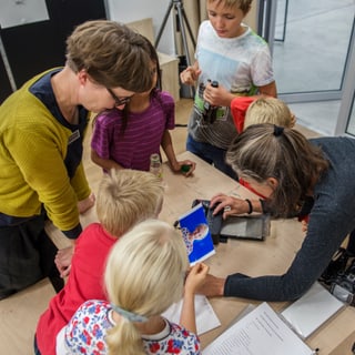 Kinder und Erwachsene betrachten ein Tablet an einem Tisch.