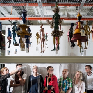 Menschen betrachten hängende Puppen in einem Ausstellungsraum.