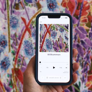 Hand hält Smartphone vor farbigem Blumengemälde.