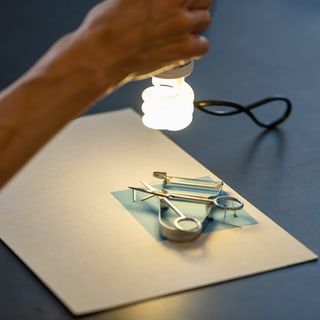 Hand hält Lampe über Solarpapier belegt mit Alltagsgegenständen.