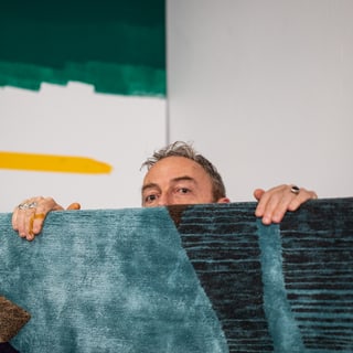 Eine Person, die hinter einem bunten Teppich hervorschaut.