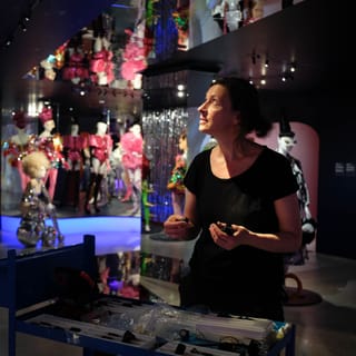 Frau in schwarzem T-Shirt in Ausstellung mit bunten Kostümen.