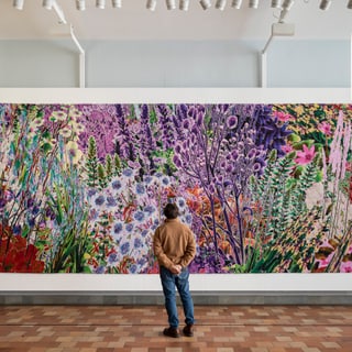 Person betrachtet ein grosses, buntes Gemälde von Blumen.