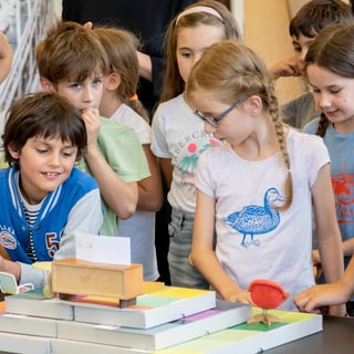 Kinder beobachten neugierig ein Projekt auf einem Tisch.