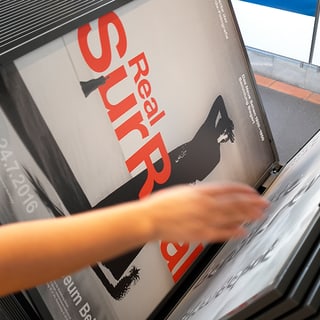 Person durchsucht Kunstplakate in einem Ständer.