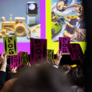 Menschen halten Schilder hoch bei einer Präsentation mit bunten Bildern im Hintergrund.