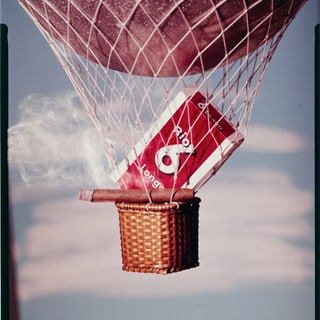 Heissluftballon mit Zigarettenschachtel und Zigarre als Korb, Rauch steigt auf.