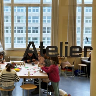 Menschen beim Basteln im Atelier, gesehen durch Glasfenster.