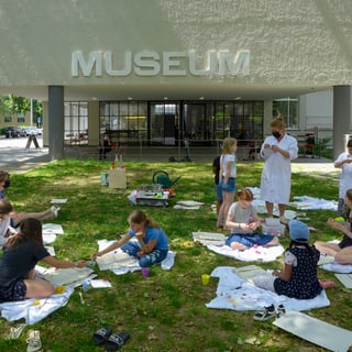 Kinder Drucken auf Rasen vor Museumseingang.