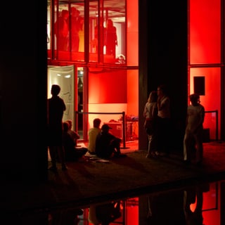 Menschen vor rot beleuchtetem Gebäude bei Nacht.