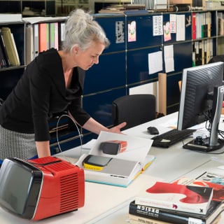 Frau betrachtet Dokumente neben vintage Fernseher im modernen Büro.