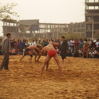Zwei Ringer auf Sandplatz von Zuschauern umgeben.