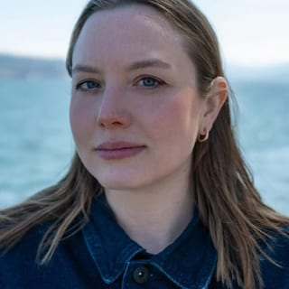 Frau mit braunem Haar vor Wasserhintergrund.