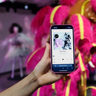Hand hält Smartphone mit Musik-App vor leuchtend rosa Kostüm.