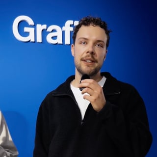 Person mit Mikrofon vor blauem Hintergrund mit Schriftzug.