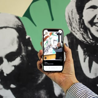 Hand hält Smartphone vor Schwarzweiss-Wandbild.