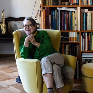 Frau im Sessel in Bücherei mit Saxophon im Hintergrund.