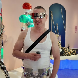 Mann mit futuristischer Brille und weissem Tanktop in bunter Umgebung.