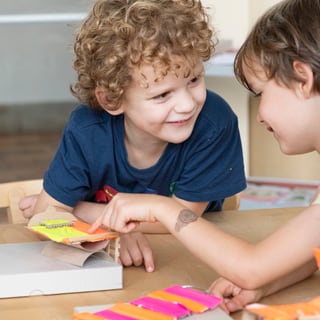 Drei Kinder basteln gemeinsam an einem Tisch.",