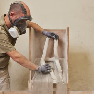 Person mit Maske arbeitet an einem Sandguss-Prozess.