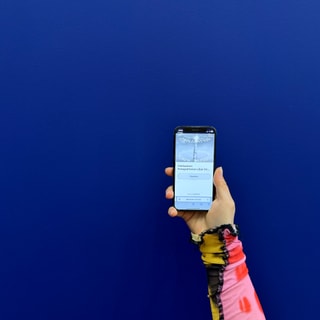 Hand hält ein Smartphone vor blauem Hintergrund.