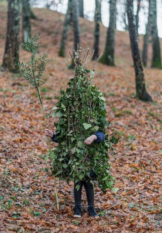 Person im Blätterkostüm in bewaldetem Gebiet.