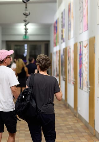 Menschen gehen durch Kunstgalerie mit Plakaten an den Wänden.