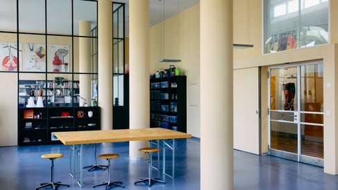 Moderner Raum mit Tisch, Hockern und Regalen, gelbe Säulen.