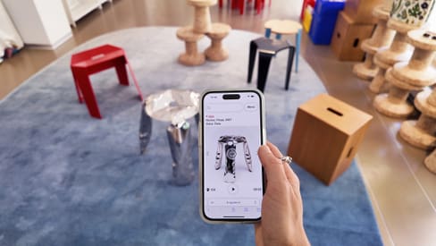 Hand hält ein Smartphone mit Musik-App im Raum mit bunten Hockern.