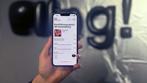 Hand hält Smartphone vor unscharfem Hintergrund mit Schriftzug 'ping!'.